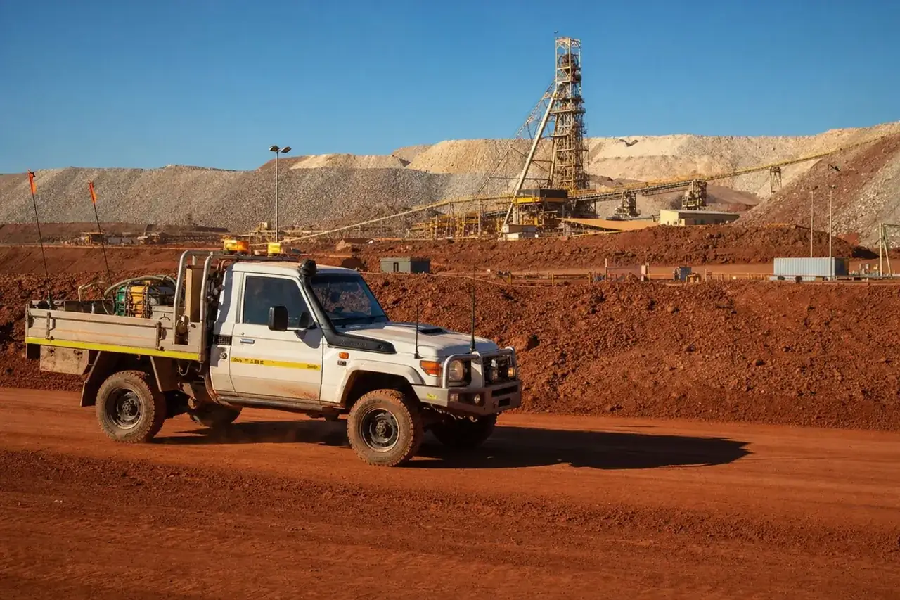 White mine-spec hotshot ute on red Goldfields dirt near Kalgoorlie with a gold-mine headframe in the distance, WA